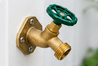 Close-up of a brass hose bib with green wheel handle mounted on the white post